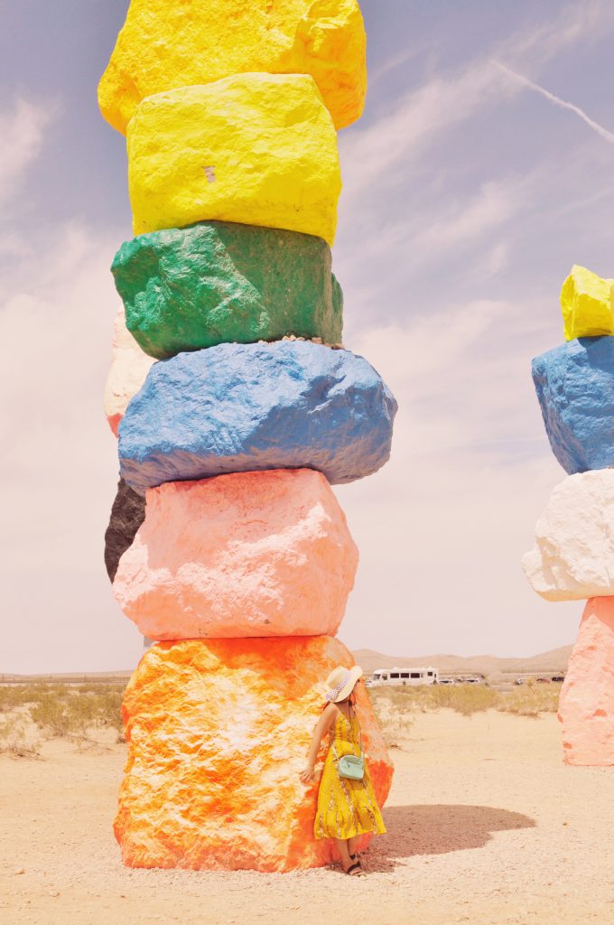 Woman stands in front of neon colored rock tower at Seven Magic Mountains