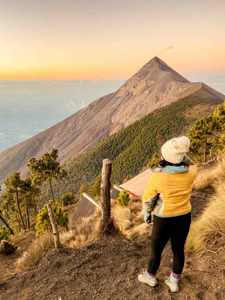 woman stands in front of view of Volcan Fuego at sunrise