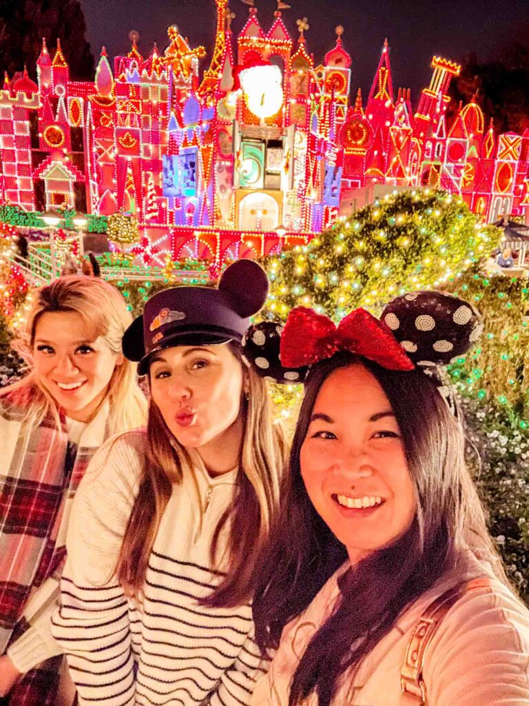 Selfie of 3 women in front of It's a Small World light display