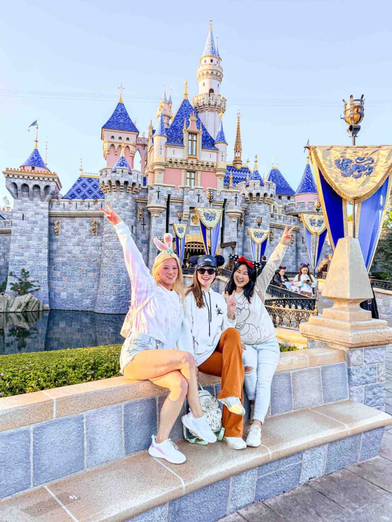 group of women posing in front of Sleeping Beauty castle throwing up peace signs